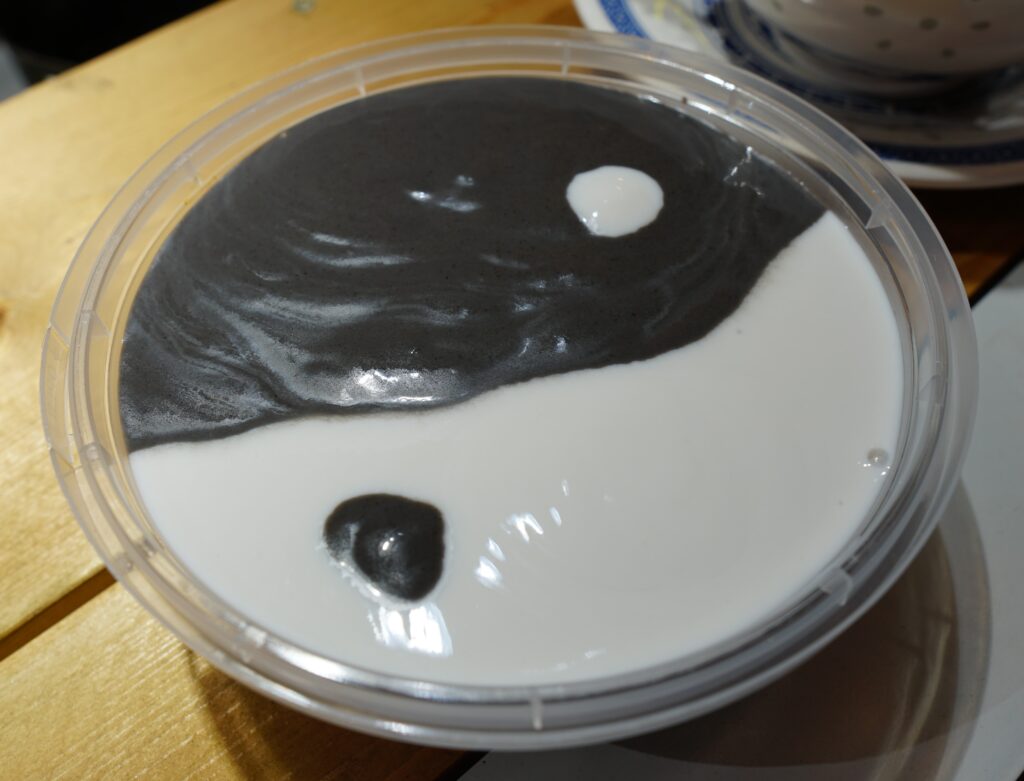 Plastic container with yin-yang symbol containing black sesame and peanut cream dessert.