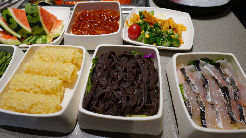 A table with a variety of food in white containers at Haidilao Hotpot in Wuhan.