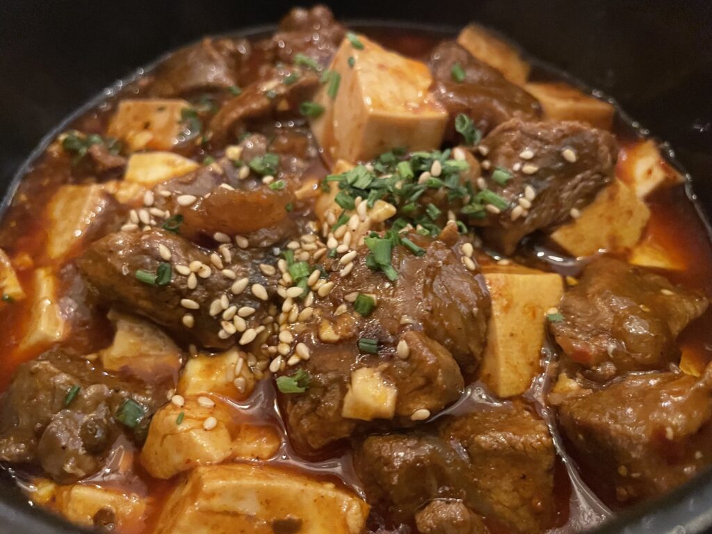 Beef and tofu simmered in a slow cooker and topped with spring onions and sesame seeds, a traditional Chinese dish from Sichuan cuisine in Munich