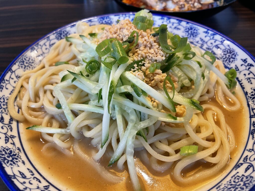 A bowl of handmade Chinese noodles with cucumber, spring onions and peanuts on a table in Frankfurt