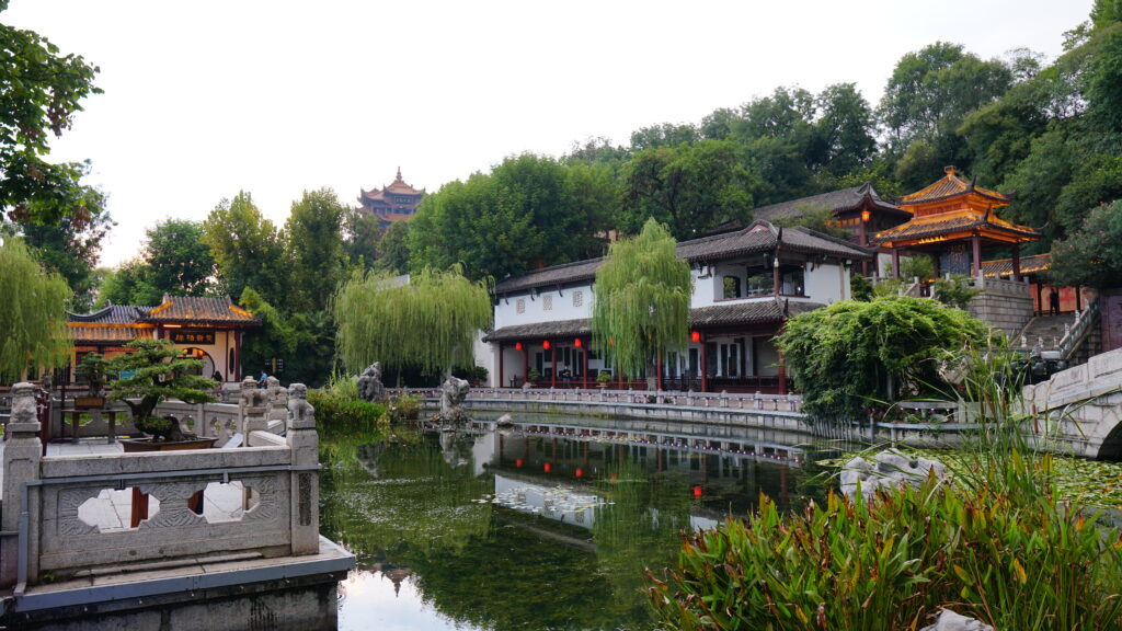 A tranquil Chinese garden pond with a bridge and statue creating a peaceful and picturesque scene of a landmark in Wuhan.