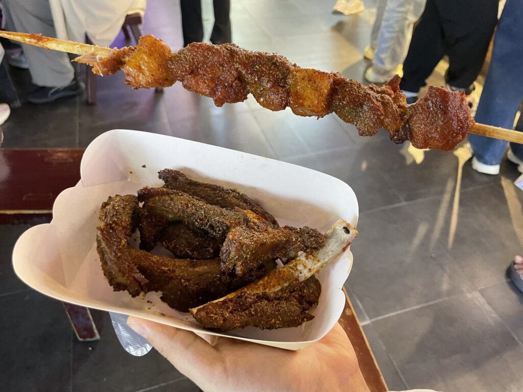 A person holds a skewered meat stick and some grilled lamb rips.