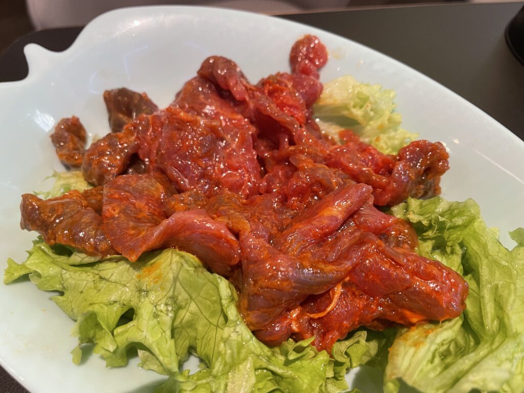 Ein Teller mit rohem Fleisch auf grünem Salat, bereit zum Kochen