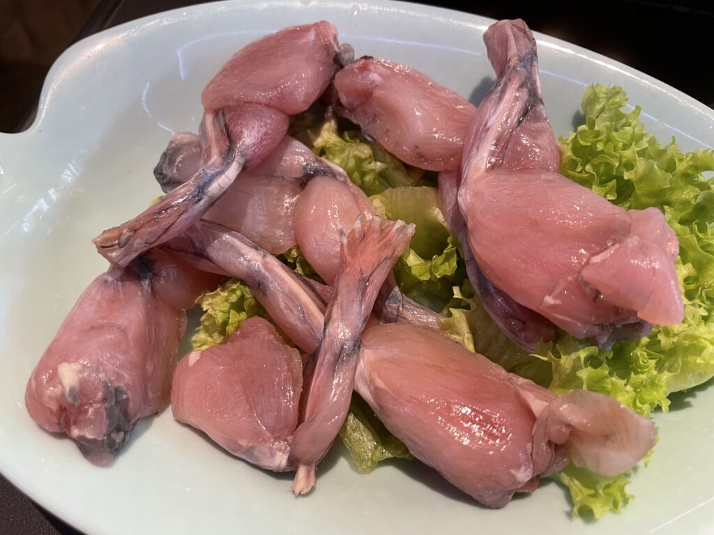 Ein Teller mit rohen Froschschenkeln auf grünem Salat, bereit zum Kochen