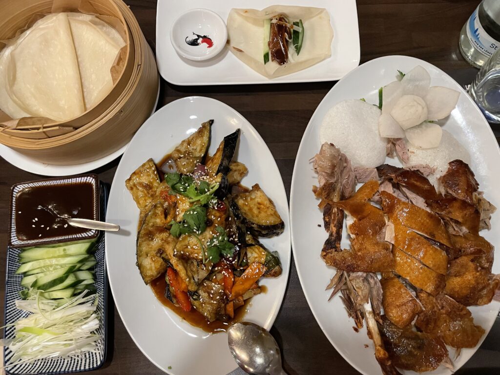 Table with plates of Authentic Peking Duck with wraps, fried eggplant and vegetables at Restaurant Yung in Frankfurt