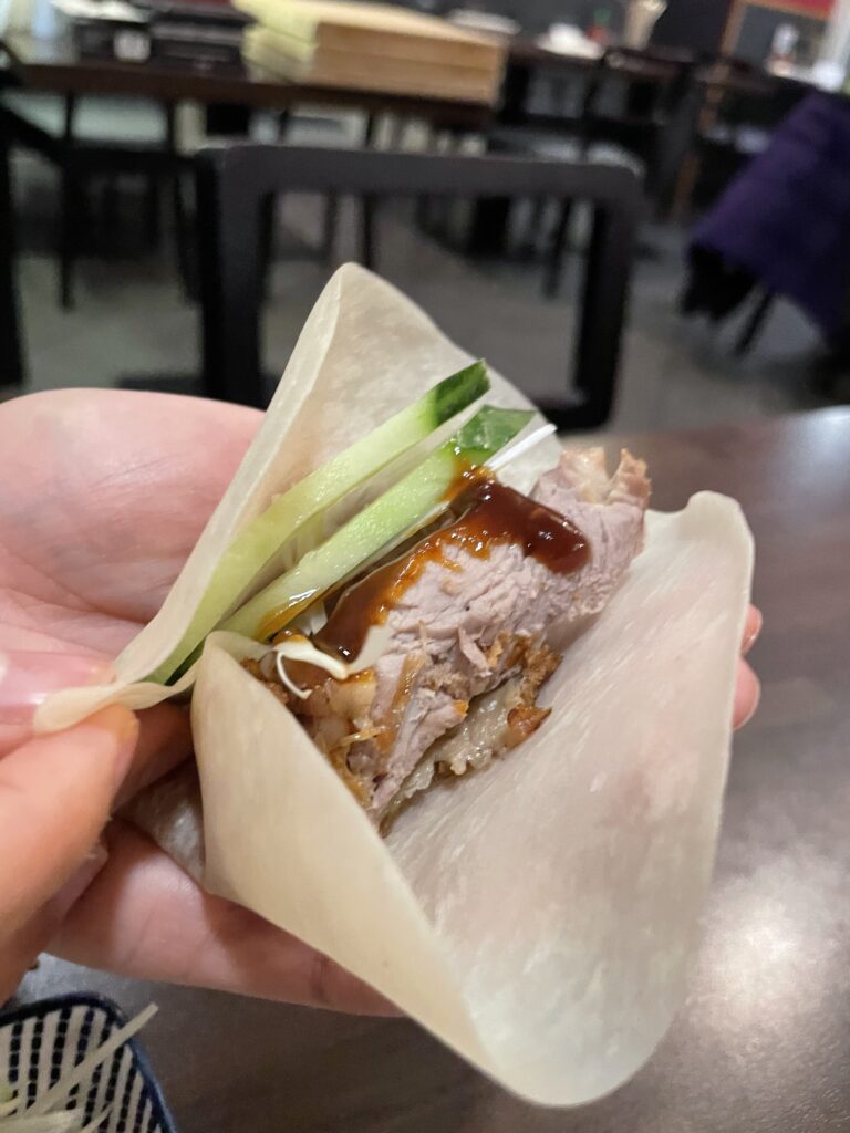 A wrapped Peking duck with a cucumber is being held by a person