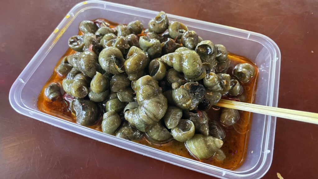 A plastic container filled with snails and some chopsticks.