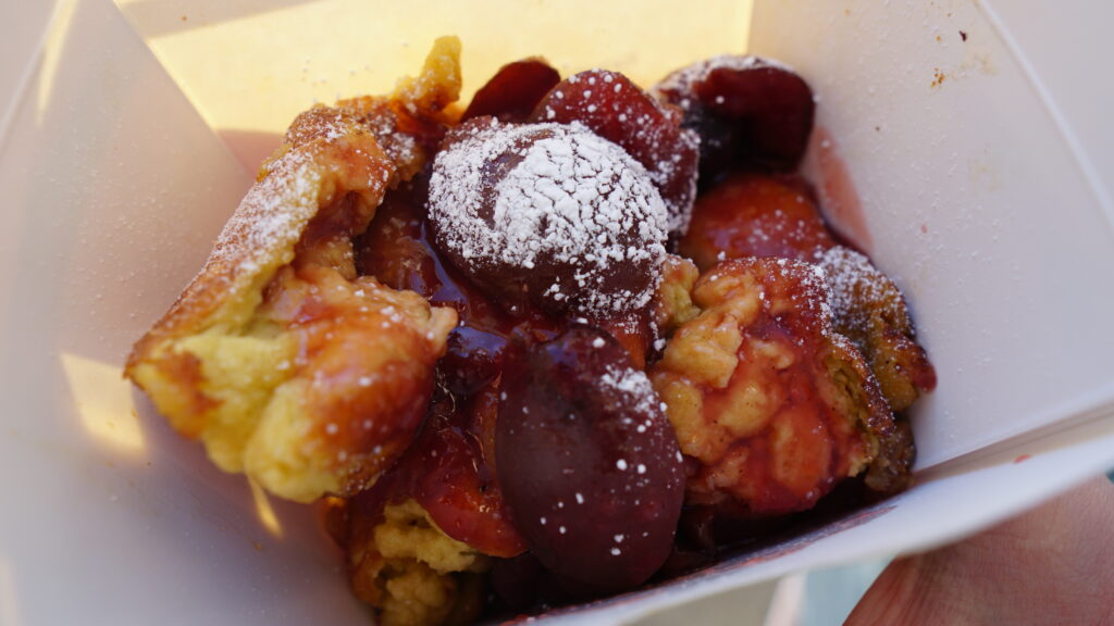 Image of a person holding a container of Kaiserschmarrn dusted with powdered sugar and topped with jam for our Vienna travel and food blog.