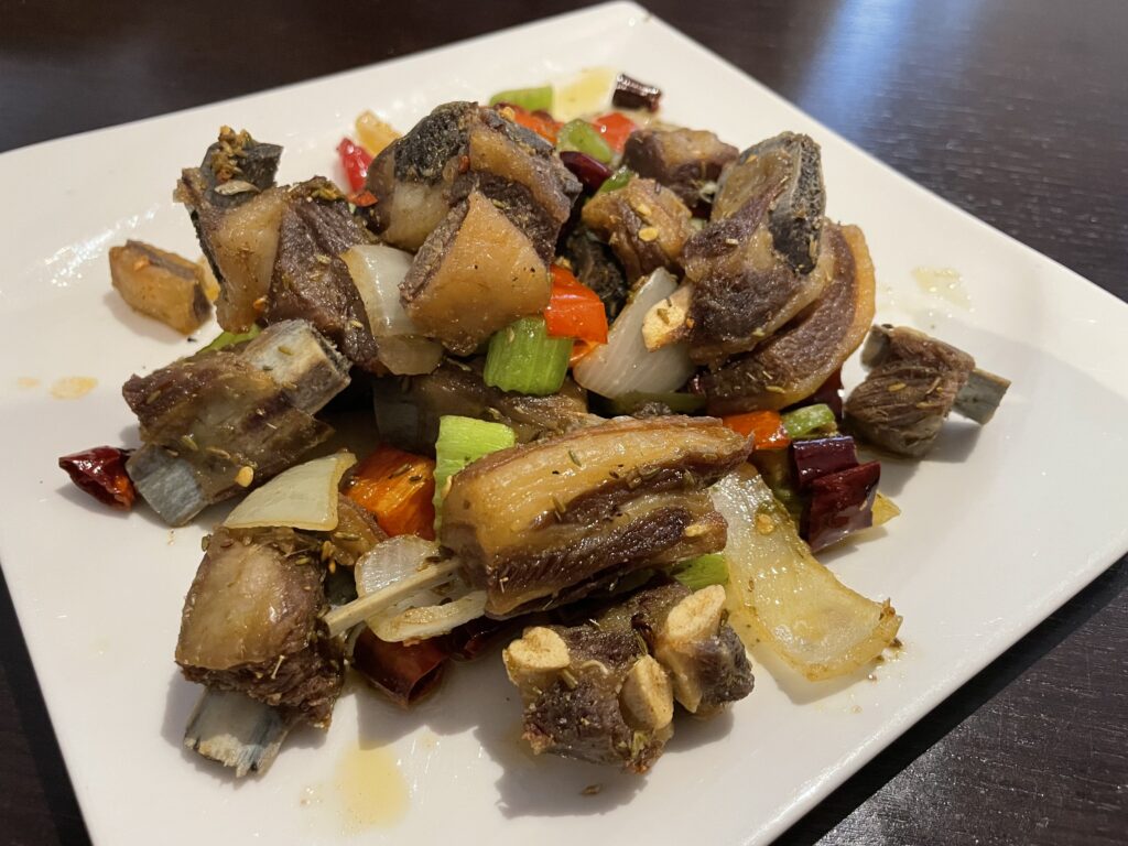 A plate of lamb ribs seasoned with cumin, accompanied by a colorful assortment of fresh vegetables, on a table at a Hunan Chinese restaurant in Frankfurt.