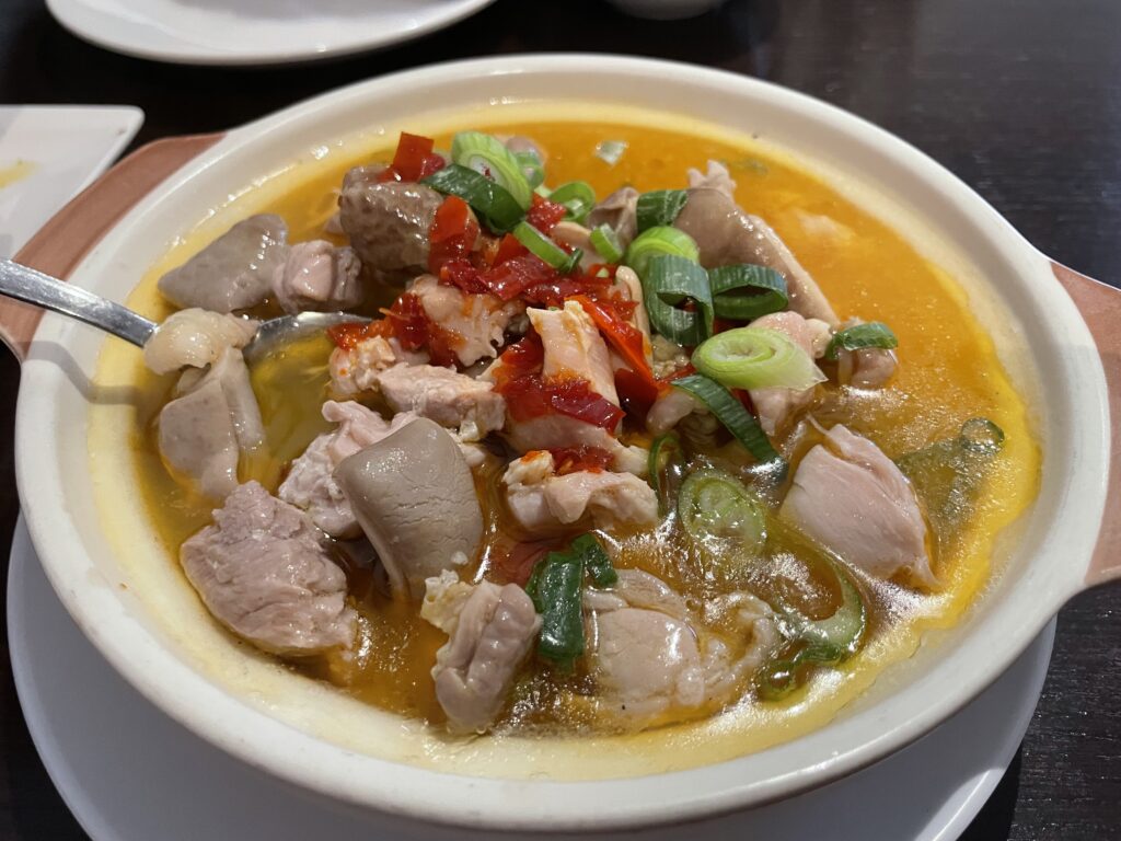 A plate with a bowl of soup containing pork stomach, chicken and pickled chili peppers, accompanied by vegetables, at a Hunan Chinese restaurant in Frankfurt.