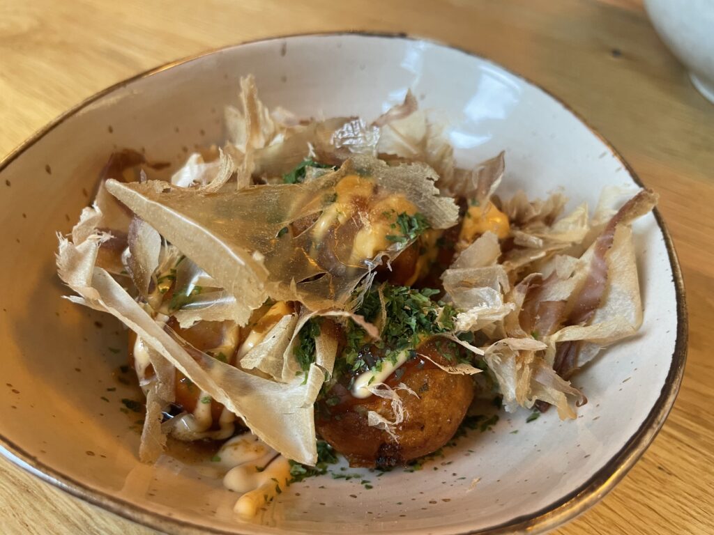 A bowl of takoyaki topped with takoyaki sauce, Japanese mayonnaise, bonito flakes and dried seaweed