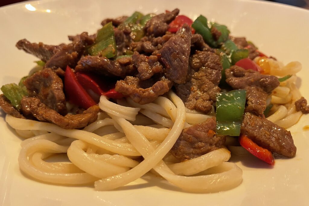 Beef, noodles and vegetables on a white plate, traditional Läghmen dish.