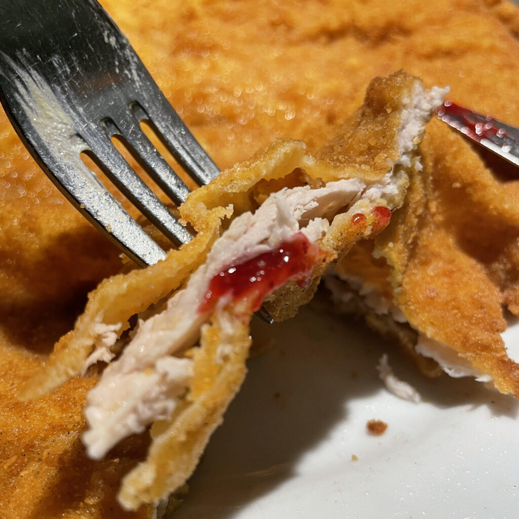 A fork piercing Wiener schnitzel with a little jam on it.