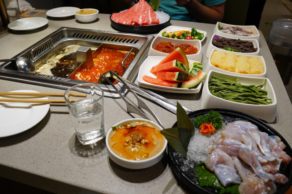 Numerous plates of food arranged on a table at Haidilao Hotpot in Wuhan.